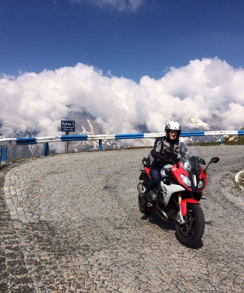 Motorrijder op hoge Alpenpas tijdens de motorreis Oostenrijk Italië Slovenië op Dag 4 (tourdag 320 km); kronkelende bergweg met wolken en vergezichten.